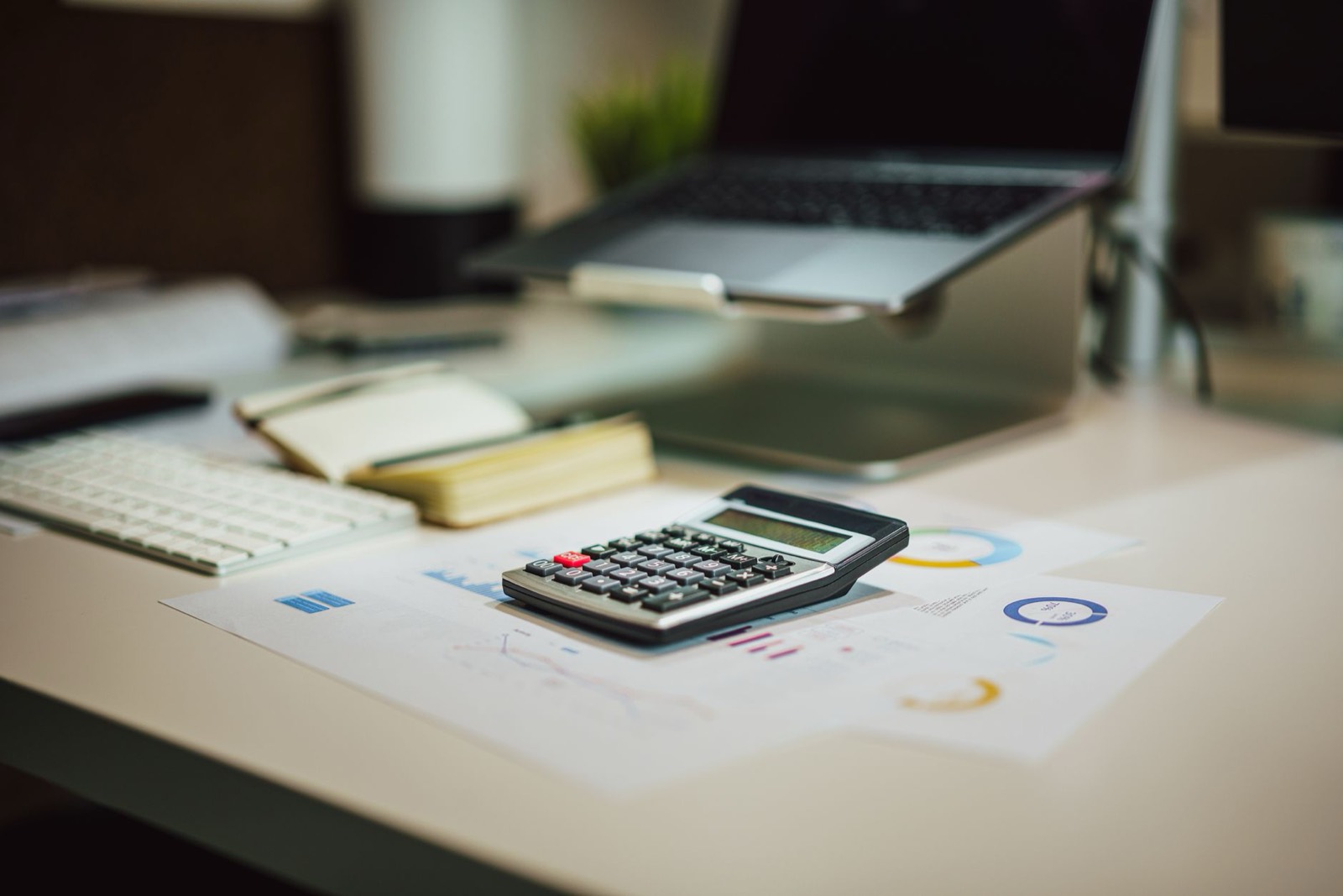 Calculatrice posée sur des graphiques devant un ordinateur portable, pour suivre les redevances d'un investissement à impact